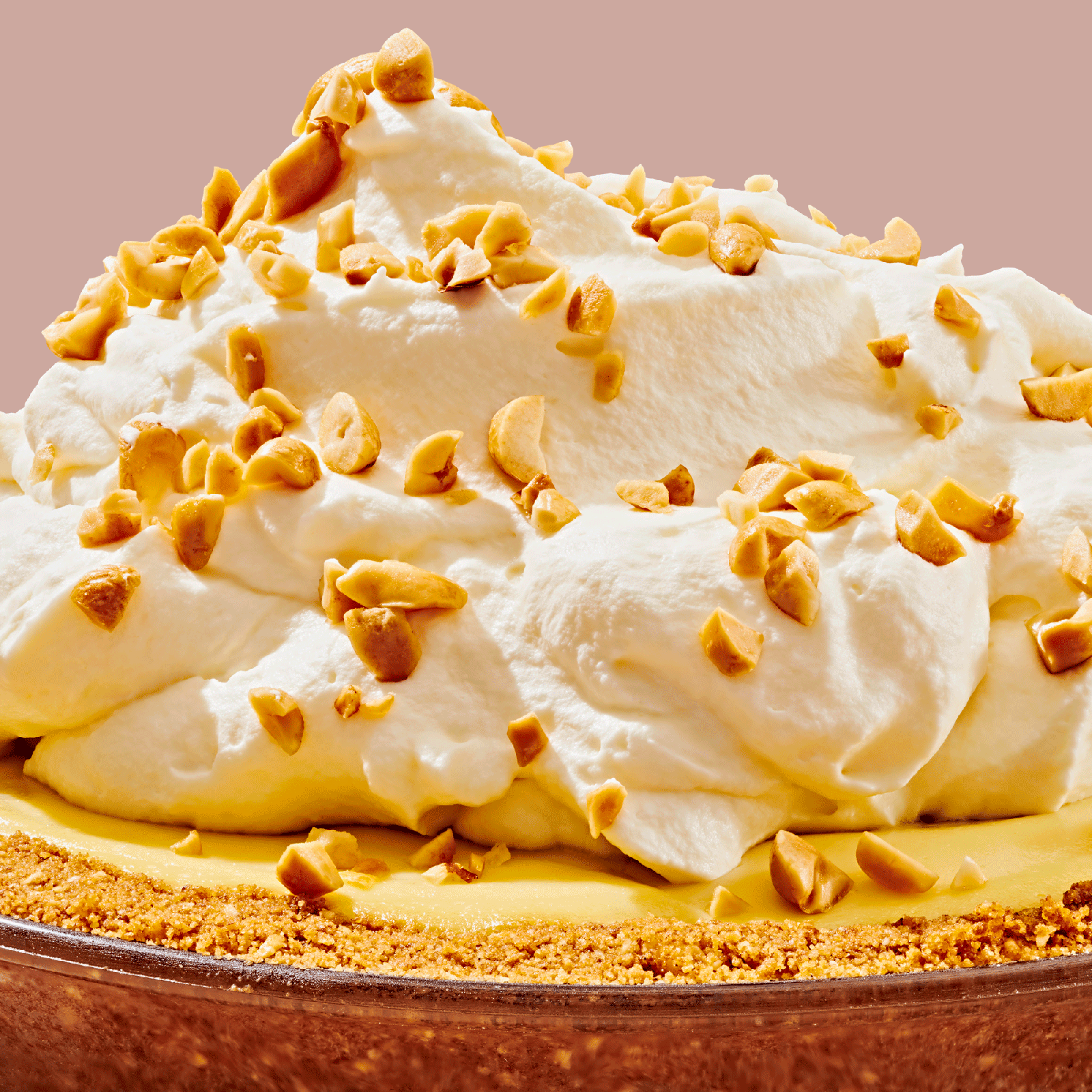 Closeup side view of a milehigh banana cream pie garnished with whipped cream and chopped peanuts.