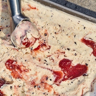 Overhead shot of semifreddo swirled with ribbons of plum being scooped out of a tray.