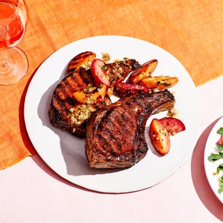 Grilled bonein pork chops and plums on a plate with arugula salad on the side.