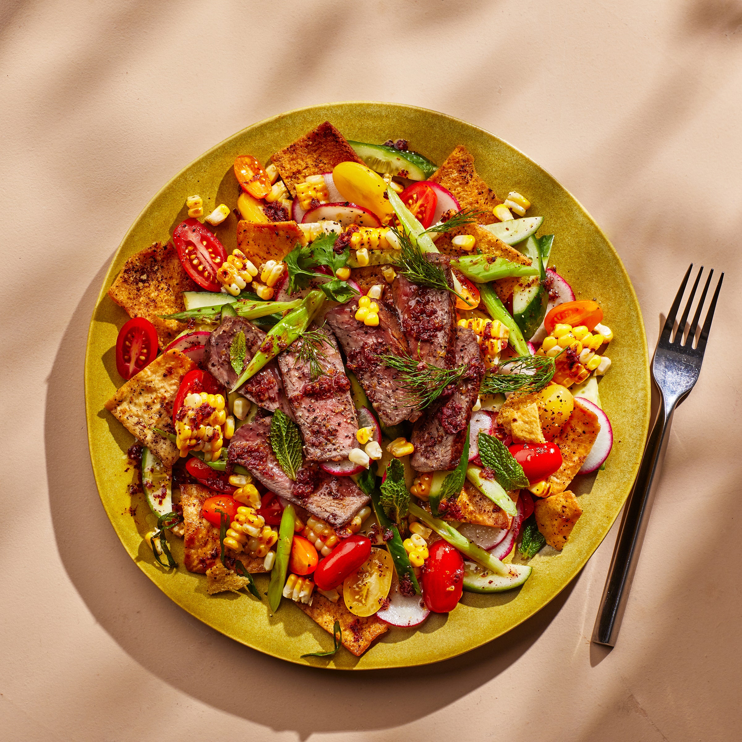 Beige surface with a yellow plate of steak fattoush.