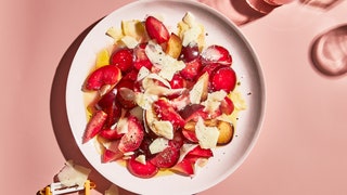 Large plated fruit salad with sliced plums and jagged Parmesan shavings topped with olive oil and black pepper.