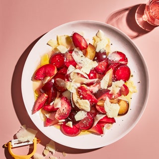 Large plated fruit salad with sliced plums and jagged Parmesan shavings topped with olive oil and black pepper.