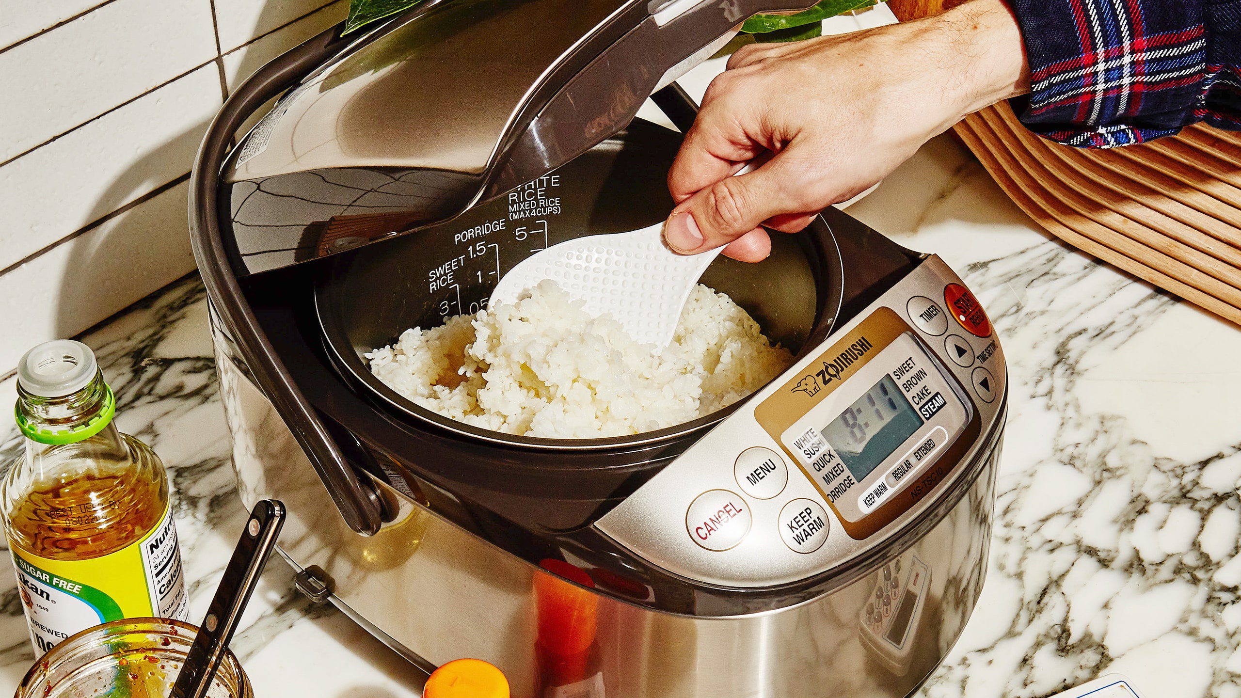 A hand scooping white rice out of a Zojirushi Rice Cooker one of the best rice cookers according to Bon Apptit