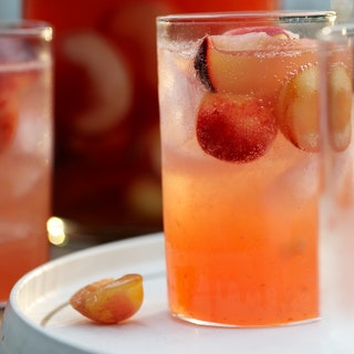 A tall glass of stone fruit sangria with cut pieces of fruit in it.